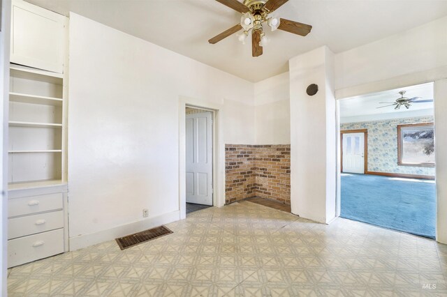 empty room with ceiling fan and brick wall