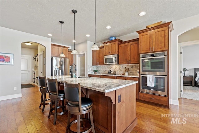 2706 E Rochester Ct, Meridian, ID 83646 - kitchen with stainless steel appliances, arched walkways, a sink, brown cabinetry, and a textured ceiling