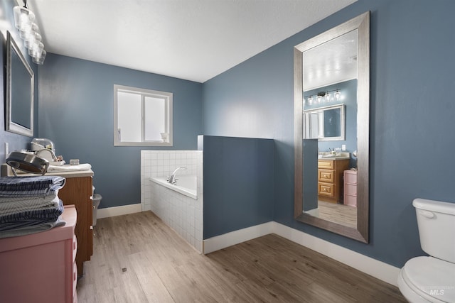 bathroom featuring vanity, hardwood / wood-style flooring, a relaxing tiled tub, and toilet