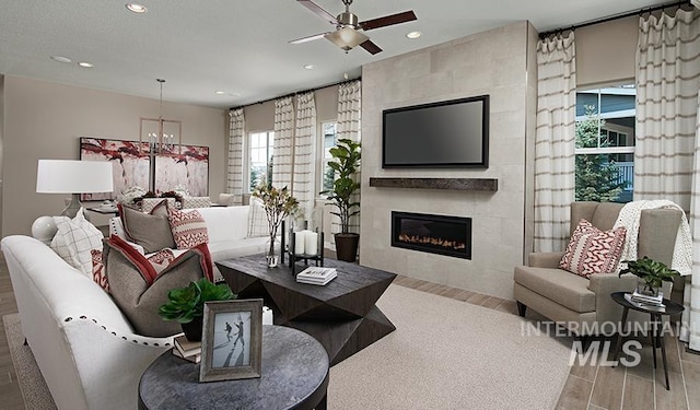 living room with wood finished floors, ceiling fan with notable chandelier, a fireplace, and recessed lighting