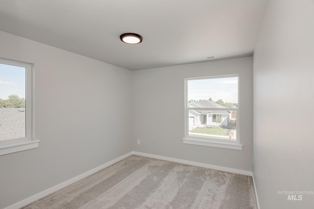 spare room featuring visible vents, light colored carpet, and baseboards