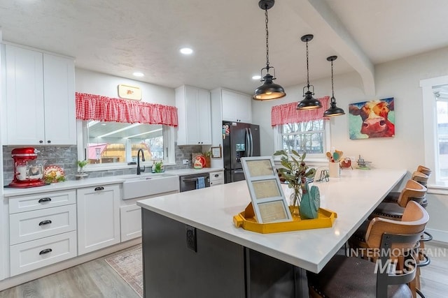 kitchen with a kitchen bar, tasteful backsplash, black fridge, and white cabinetry