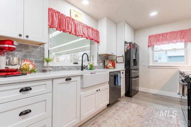 kitchen with white cabinetry, sink, light hardwood / wood-style floors, decorative backsplash, and appliances with stainless steel finishes