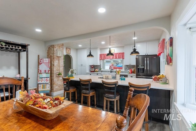 kitchen featuring stainless steel fridge, a kitchen breakfast bar, wood-type flooring, decorative light fixtures, and white cabinets