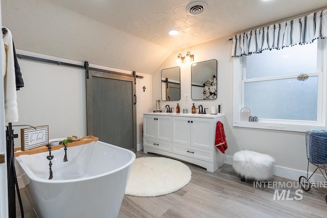 bathroom with hardwood / wood-style flooring, vanity, a bath, and vaulted ceiling