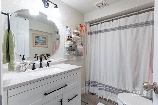 bathroom with hardwood / wood-style floors, vanity, a shower with curtain, toilet, and a textured ceiling