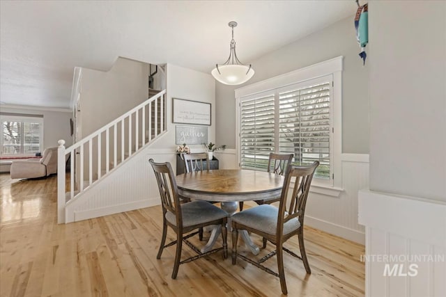 dining room featuring stairway, a decorative wall, light wood-style flooring, and a wainscoted wall