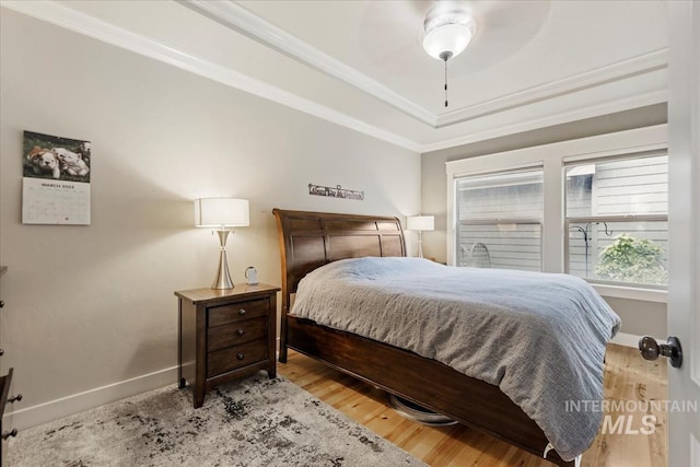 bedroom featuring baseboards, crown molding, a tray ceiling, and wood finished floors