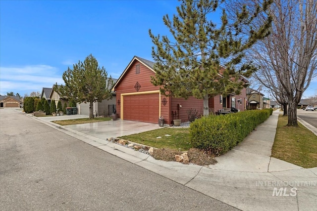 view of property hidden behind natural elements with a residential view, an attached garage, and concrete driveway