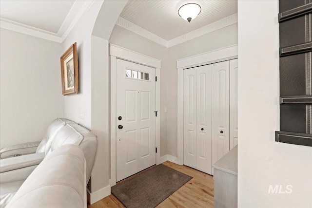 entryway with arched walkways, light wood-style floors, and ornamental molding