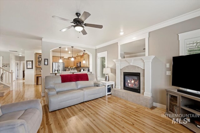 living area featuring crown molding, baseboards, light wood-type flooring, a tile fireplace, and a ceiling fan