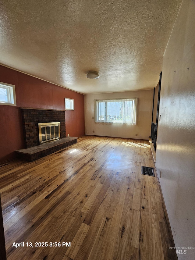 314 S Phillippi St, Boise, ID 83705 - unfurnished living room featuring light wood finished floors, a textured ceiling, plenty of natural light, and a brick fireplace