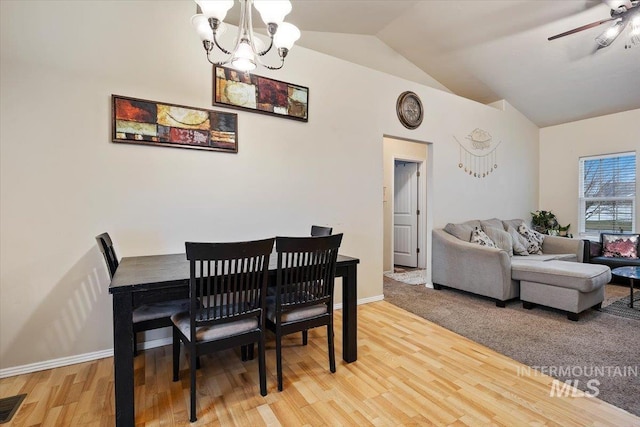 dining area with ceiling fan with notable chandelier, light hardwood / wood-style floors, and vaulted ceiling