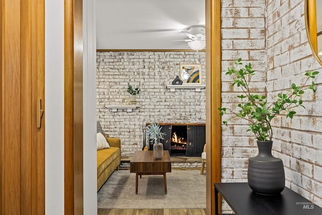 sitting room with a ceiling fan, a brick fireplace, wood finished floors, and brick wall