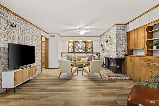 living room with crown molding, light wood finished floors, a brick fireplace, a ceiling fan, and visible vents