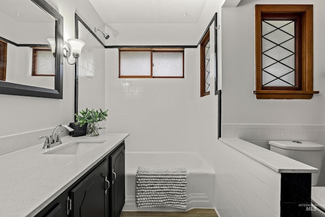 bathroom featuring wainscoting, vanity, toilet, tile walls, and tub / shower combination