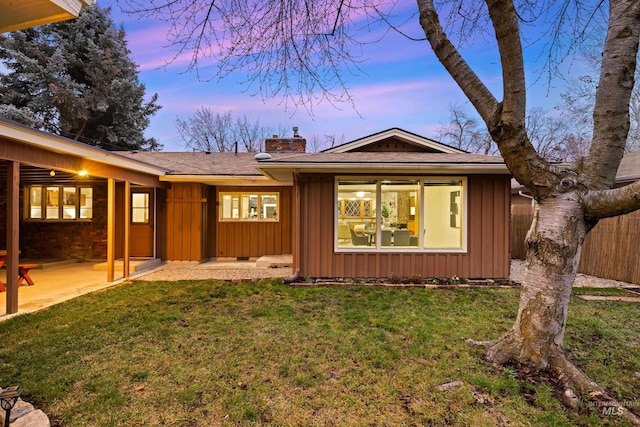 rear view of property with a lawn, board and batten siding, a patio area, and a chimney