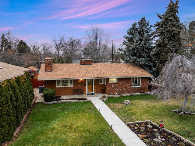 ranch-style home with roof with shingles, a front lawn, brick siding, a porch, and a chimney