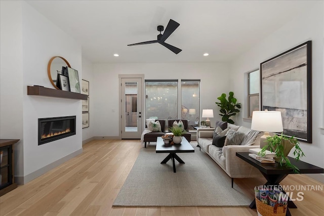 living room featuring baseboards, recessed lighting, light wood-style flooring, a glass covered fireplace, and a ceiling fan