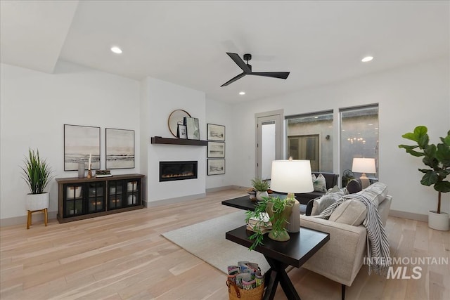 living room with a glass covered fireplace, wood finished floors, recessed lighting, baseboards, and ceiling fan