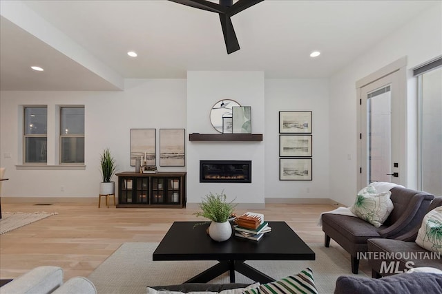 living area featuring a glass covered fireplace, recessed lighting, light wood-type flooring, and baseboards