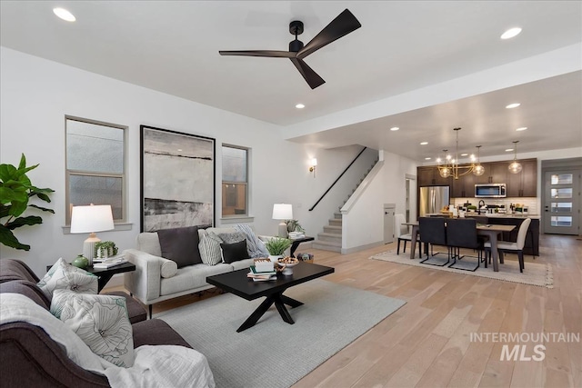 living room with stairs, ceiling fan with notable chandelier, recessed lighting, and light wood-type flooring