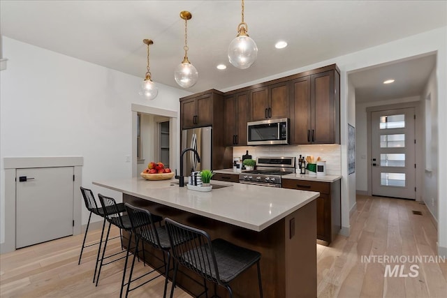 kitchen featuring a kitchen bar, a sink, appliances with stainless steel finishes, decorative backsplash, and dark brown cabinets