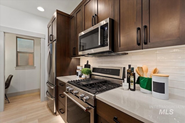 kitchen featuring baseboards, dark brown cabinetry, light wood-type flooring, decorative backsplash, and stainless steel appliances