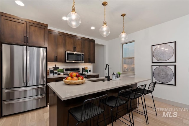 kitchen featuring dark brown cabinetry, a breakfast bar area, light countertops, decorative backsplash, and stainless steel appliances