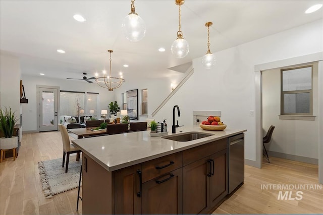 kitchen with a center island with sink, a sink, stainless steel dishwasher, light wood-style floors, and light countertops