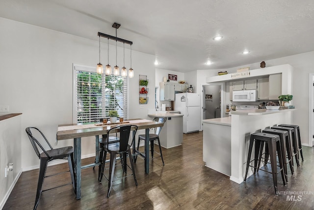 kitchen featuring a peninsula, light countertops, white appliances, and dark wood finished floors
