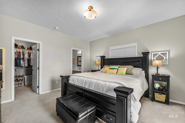 bedroom with baseboards, a closet, a spacious closet, light carpet, and ensuite bath