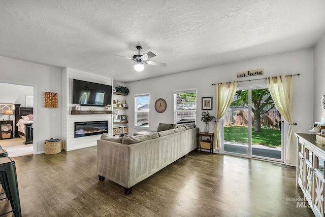living area with dark wood-type flooring, a textured ceiling, ceiling fan, and a large fireplace