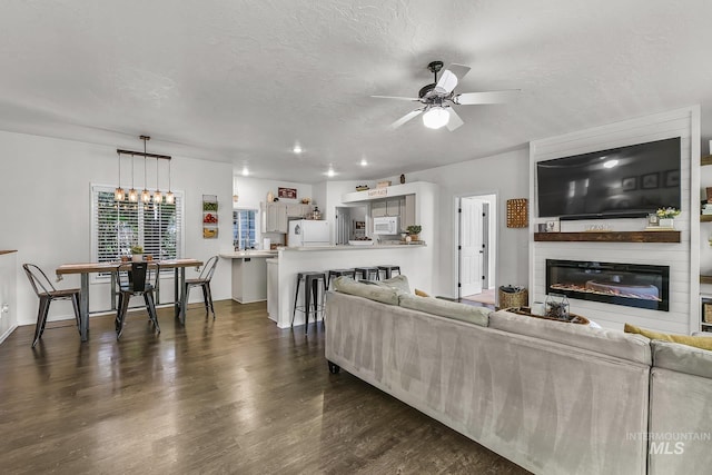 living area featuring a ceiling fan, dark wood finished floors, a glass covered fireplace, and a textured ceiling