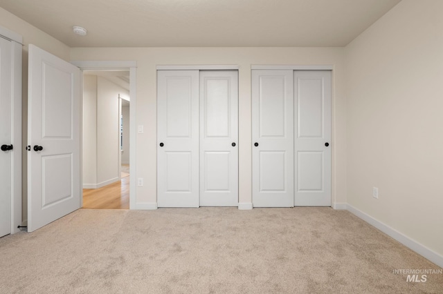 unfurnished bedroom with light colored carpet and multiple closets