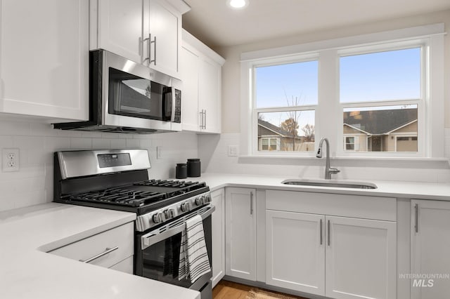 kitchen with sink, light hardwood / wood-style flooring, tasteful backsplash, white cabinetry, and stainless steel appliances