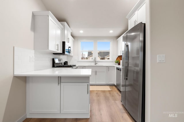 kitchen featuring kitchen peninsula, stainless steel appliances, sink, white cabinets, and light hardwood / wood-style floors