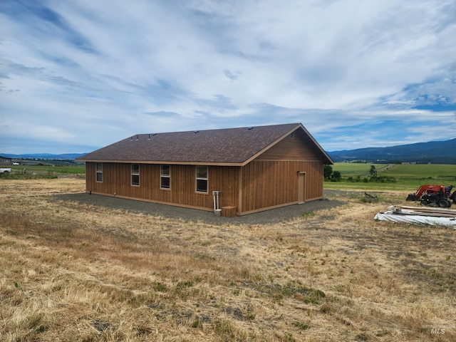 rear view of house featuring a rural view, a mountain view, and roof with shingles