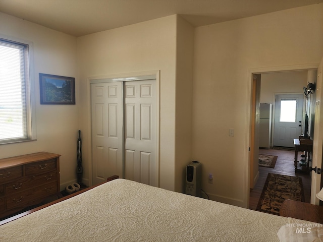 unfurnished bedroom featuring dark wood-style floors, a closet, freestanding refrigerator, and baseboards