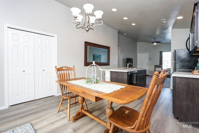 dining area featuring sink, vaulted ceiling, a textured ceiling, light hardwood / wood-style floors, and ceiling fan with notable chandelier