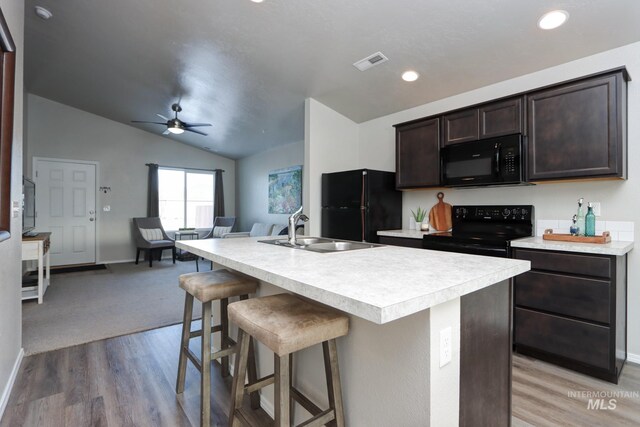 kitchen featuring lofted ceiling, sink, a breakfast bar area, black appliances, and an island with sink