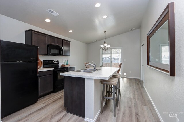 kitchen with sink, decorative light fixtures, light hardwood / wood-style flooring, a center island with sink, and black appliances