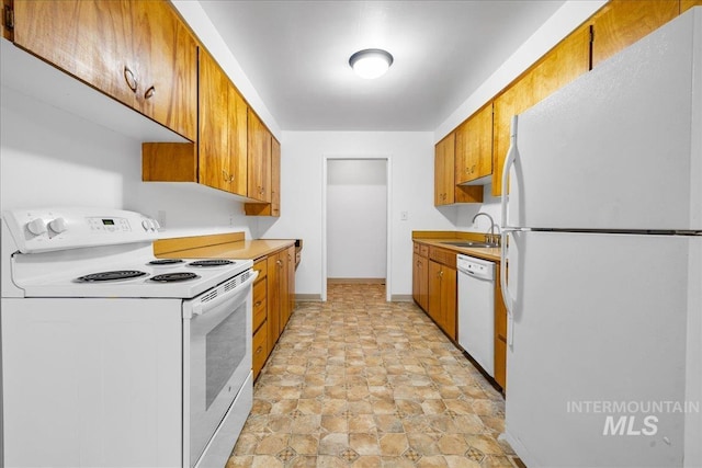 kitchen featuring brown cabinets, a sink, white appliances, light countertops, and baseboards