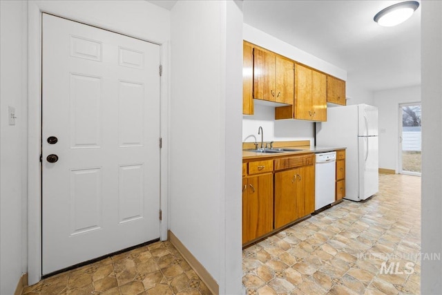 kitchen with white appliances, baseboards, a sink, light countertops, and stone finish floor