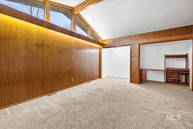 interior space with beam ceiling, visible vents, wood walls, and carpet