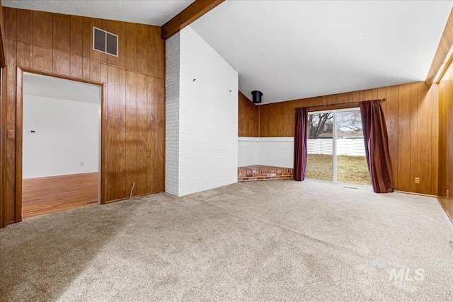 spare room featuring visible vents, beam ceiling, a textured ceiling, wood walls, and carpet flooring