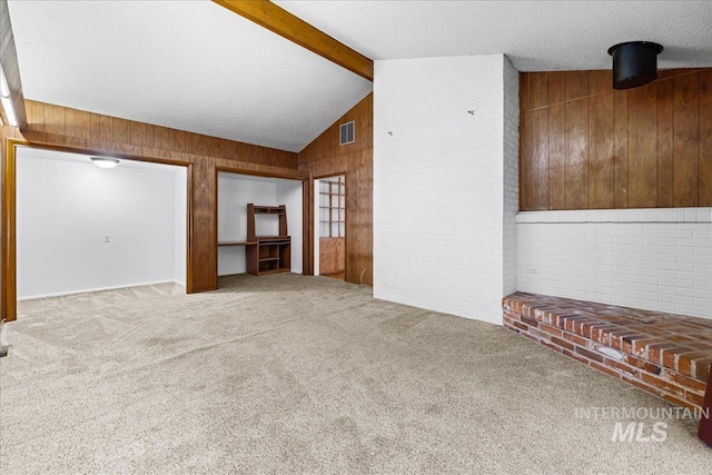 unfurnished living room featuring wooden walls, carpet, visible vents, brick wall, and vaulted ceiling with beams