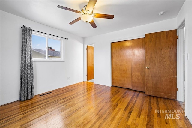 unfurnished bedroom with a closet, visible vents, a ceiling fan, and wood finished floors