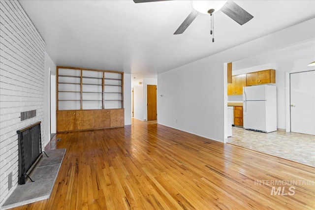 unfurnished living room with a brick fireplace, a ceiling fan, and light wood finished floors