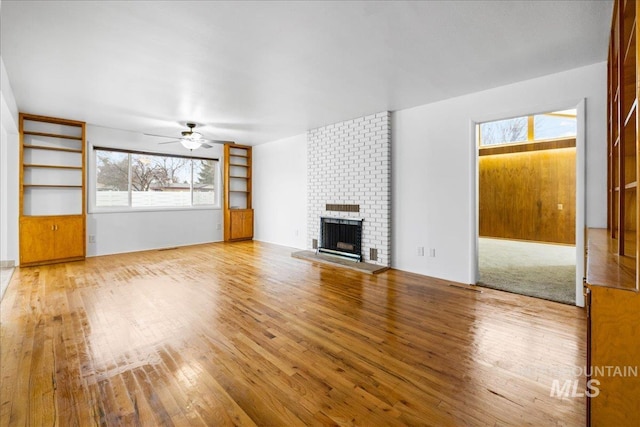 unfurnished living room featuring built in shelves, a ceiling fan, a fireplace, and hardwood / wood-style flooring